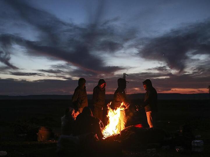 Migranten wärmen sich in der Nähe eines Grenzübergangs an einem Lagerfeuer.