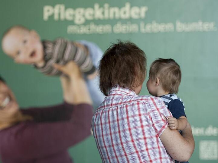 Eine Frau steht mit einem Kind vor einem Plakat mit der Aufschrift "Pflegekinder machen dein Leben bunter". Foto: Marc Tirl/Archiv