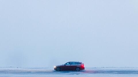 Ein Auto fährt bei dichtem Nebel über eine schneebedeckte Straße.