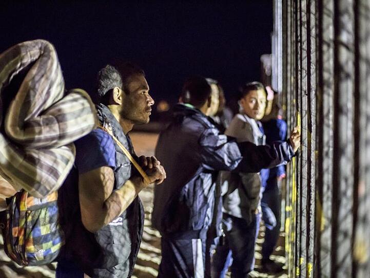 Migranten mit Matratzen und Rucksäcken am Zaun der Grenze zwischen USA und Mexiko.