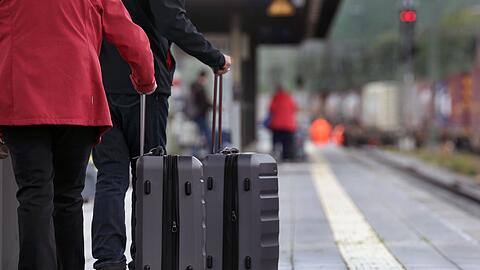 Reisende mit Koffern stehen im Hauptbahnhof an einem Bahnsteig.