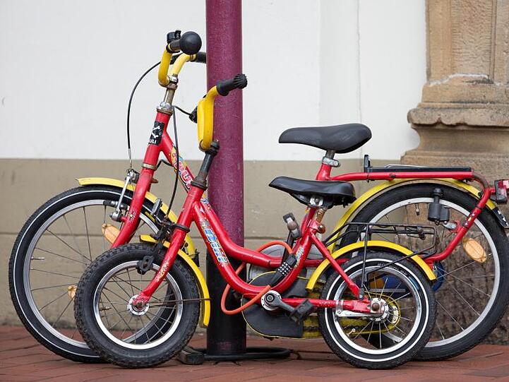 Zwei zusammengeschlossene Kinderfahrräder an einer Straßenlaterne. In Mailand hat ein Sechsjähriger von der Polizei eine neues Rad bekommen.