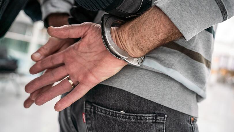 Ein Polizist führt einen Verdächtigen in Handschellen ab. (Symbolbild)