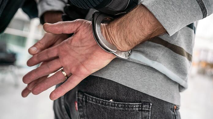 Ein Polizist führt einen Verdächtigen in Handschellen ab. (Symbolbild)