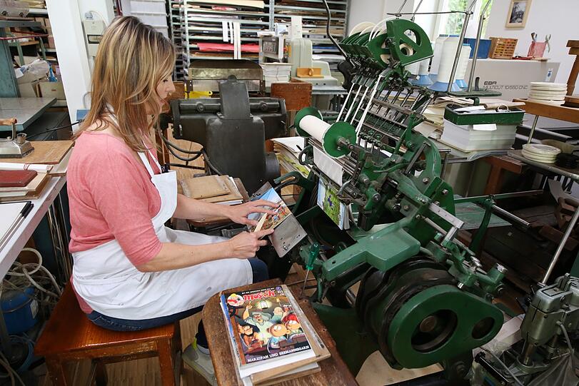 Andrea Fellinger sitzt an einer über hundert Jahre alten Maschine aus Leipzig. Hier bindet sie Comics aus der ehemaligen DDR.