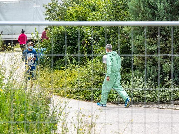Ein Mann in Schutzanzug geht hinter einem Zaun. Foto: Armin Weigel/dpa