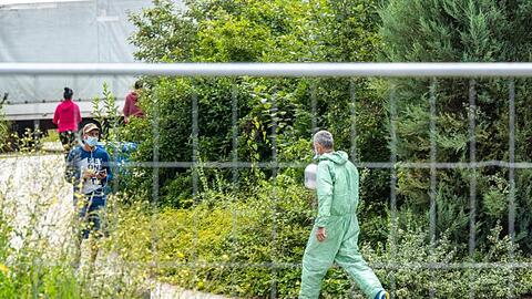 Ein Mann in Schutzanzug geht hinter einem Zaun. Foto: Armin Weigel/dpa
