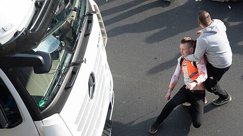 Ein Mann zerrt einen Aktivisten der Gruppe Letzte Generation während einer Blockade auf der Stadtautobahn A100 in Berlin von der Straße.