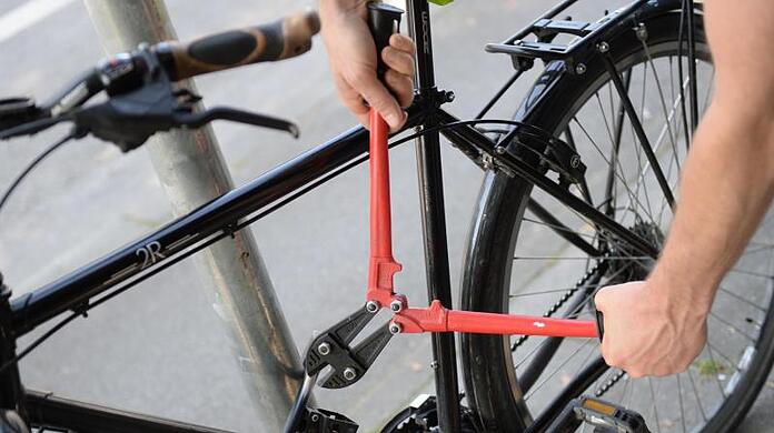 Ein Mann versucht mit einem Bolzenschneider ein Fahrradschloss aufzubrechen (gestellte Szene). Foto: Andreas Gebert/dpa/Illustration