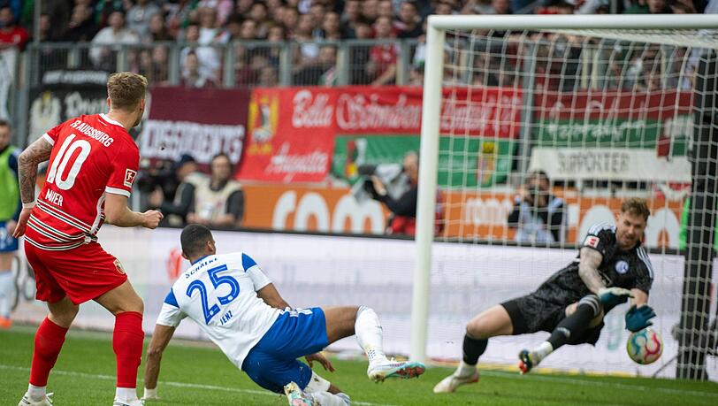 Schalkes Torwart Ralf Fährmann (r) und Moritz Jenz können das Tor von Augsburgs Arne Maier (l) nicht verhindern.