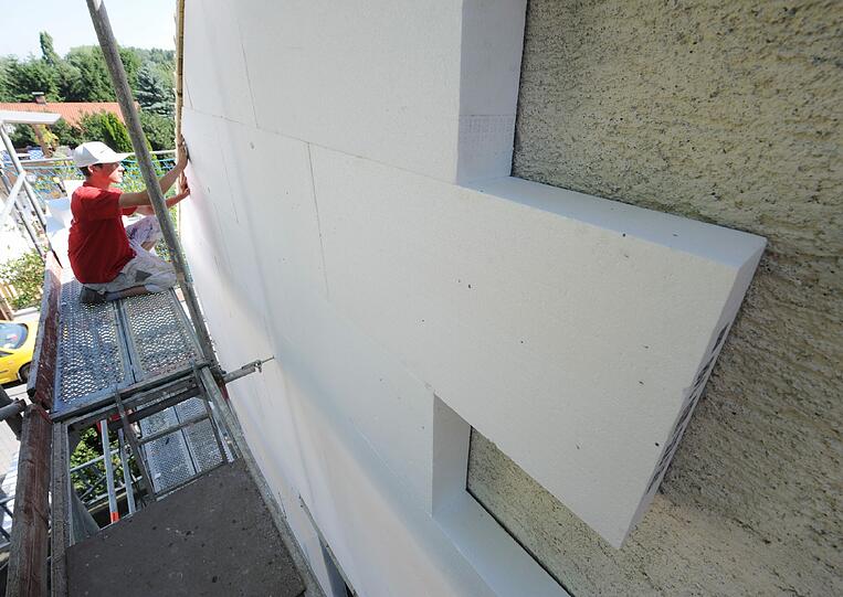 Ein Arbeiter befestigt eine Styroporplatte zur Wärmedämmung an einer Hausfassade. (Archivbild)