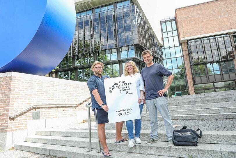 Sie wollen Künstler zusammenbringen und den leerstehenden Gasteig sinnvoll nutzen: (v.l.) Projektleiter Christian Kiesler (l.), Mitarbeiterin Sarah-Marie Scholz und Gesellschafter Till Hofmann von der Fat Cat gGmbH stehen vor dem Gasteig und zeigen das Werbeplakat für die Eröffnungsveranstaltung am Sonntag.