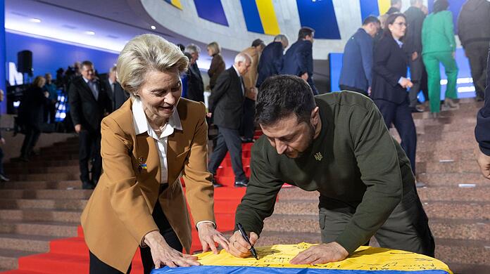 Wolodymyr Selenskyj und Ursula von der Leyen schreiben ihre Wünsche auf eine ukrainische Flagge.