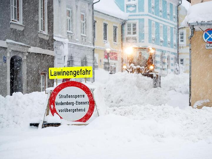 Ein Räumfahrzeug räumt eine Straße. Im Vordergrund steht ein Schild, das auf Lawinengefahr hinweist. Foto: Erwin Scheriau/APA