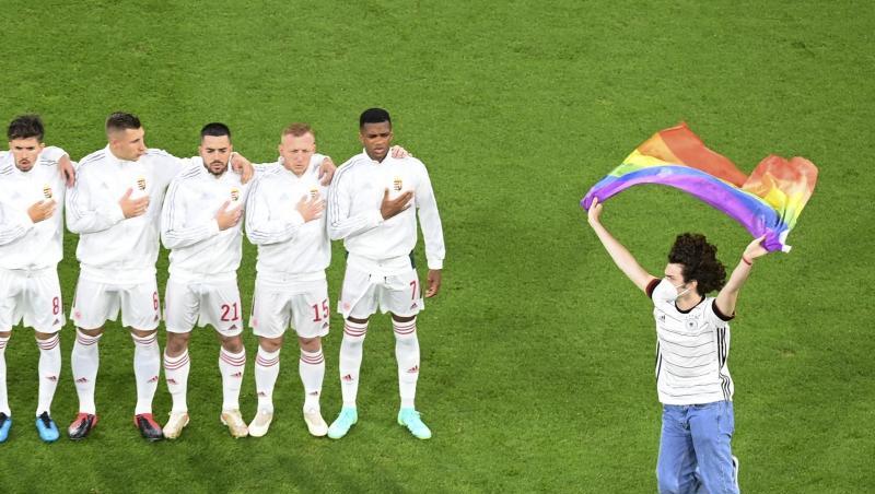 Ein junger Mann rennt mit einer Regenbogenfahne über das Spielfeld. Ein junger Mann rennt mit einer Regenbogenfahne über das Spielfeld.