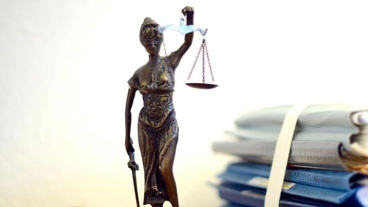 Die modellhafte Nachbildung der Justitia steht neben einem Holzhammer und einem Aktenstapel. Foto: Volker Hartmann/dpa/Archivbild