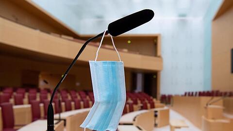 Ein Mund-Nase-Schutz hängt im Plenarsaal im bayerischen Landtag an einem Mikrofon. Foto: Sven Hoppe/dpa/Archiv/Illustration