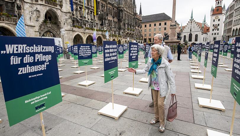 Passanten schauen sich die auf dem Marienplatz aufgestellten Plakate zur Kampagne "Nächstenpflege" des VdK an.