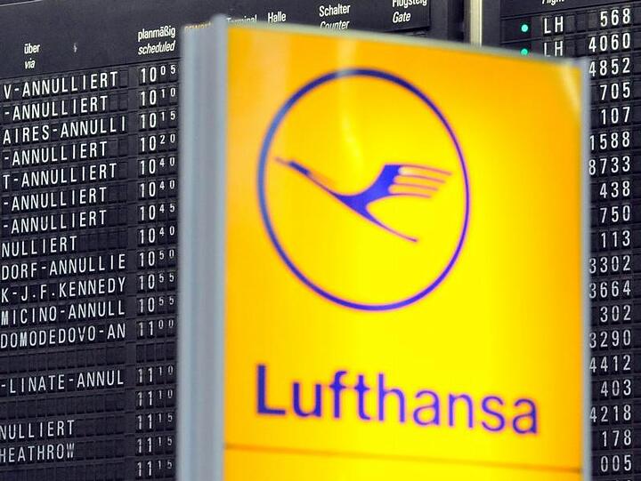 Ein Lufthansa-Logo vor einer Anzeigetafel, auf der zahlreiche Flüge annulliert sind.