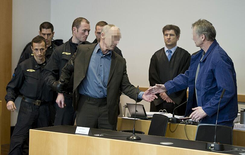 Die wegen Mordes an einem Polizisten angeklagten Raimund M. (vorne, l.) und Rudolf R. (vorne, r.) in Augsburg vor Gericht. Die Beschuldigten müssen Fußfesseln tragen