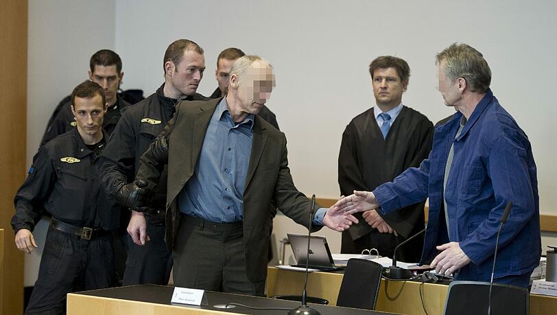 Die wegen Mordes an einem Polizisten angeklagten Raimund M. (vorne, l.) und Rudolf R. (vorne, r.) in Augsburg vor Gericht. Die Beschuldigten müssen Fußfesseln tragen Die wegen Mordes an einem Polizisten angeklagten Raimund M. (vorne, l.) und Rudolf R. (vorne, r.) in Augsburg vor Gericht. Die Beschuldigten müssen Fußfesseln tragen