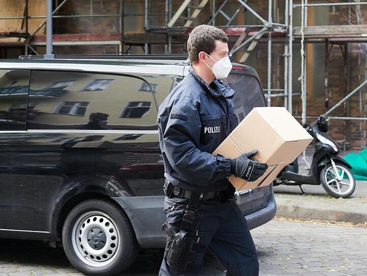 Ein Polizist trägt sichergestelltes Beweismaterial zu einem Auto.