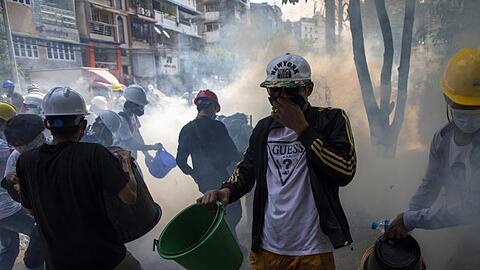 Demonstranten mit Helmen und Mund-Nasen-Schutz versuchen, rauchende Tränengaskanister mit Wasser zu löschen.