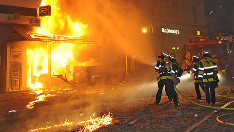 Flammen schlagen aus den Häusern in der Feilitzschstraße, auf dem Boden liegt Stroh, die Feuerwehr löscht.