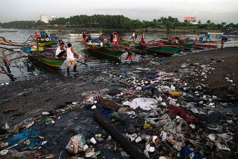 Fischer ziehen auf den Philippinen ihren Fang an Land. Umringt von Plastikmüll; Wissenschaftler prognostizieren, dass im Jahr 2050 mehr Müll als Fische in den Weltmeeren schwimmen wird.