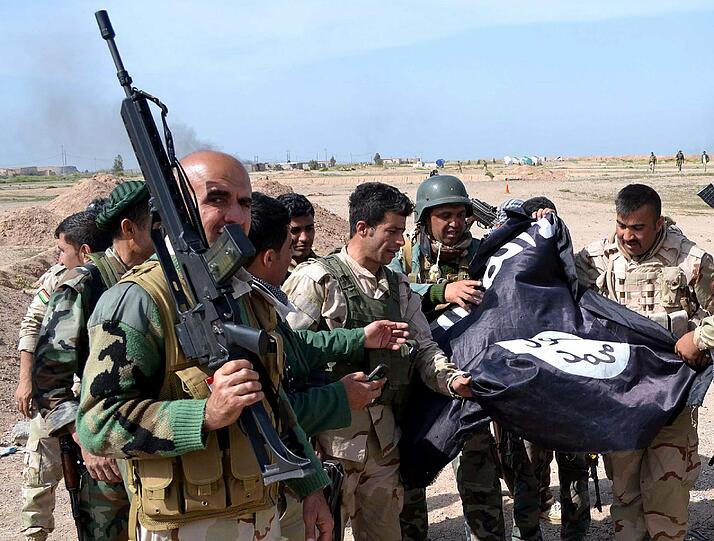 Kurdische Kämpfer präsentieren eine erbeutete Flagge der Terrormiliz IS.