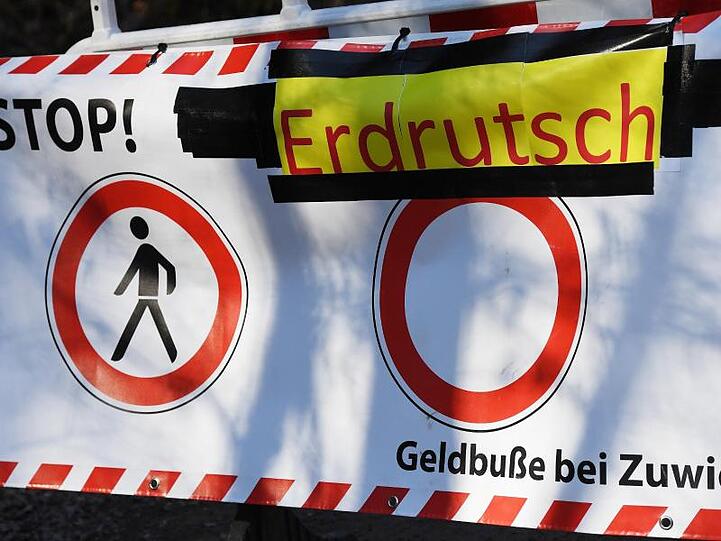 "Stop Erdrutsch" steht auf einer Wegsperre auf dem Winterweg zum Berggasthof Neureuth oberhalb von Tegernsee. Foto: Angelika Warmuth/dpa/Archivbild
