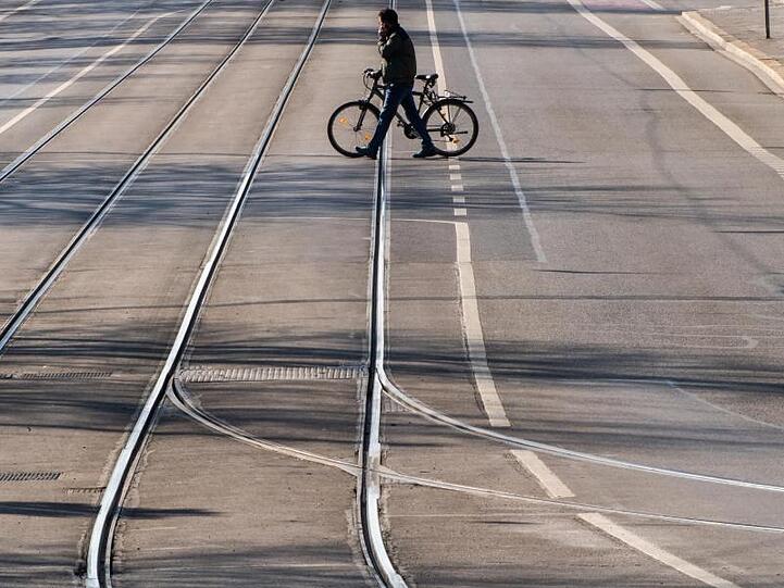 Ein Mann überquert mit einem Fahrrad eine leere Straße in München. Foto: Peter Kneffel/dpa/Archivbild