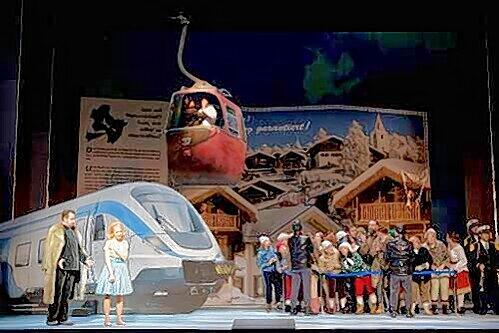 Unten der Sonderzug mit Sarastro und Pamina (Guido Jentjens, Heidi Elisabeth Meier), drüber die Gondel mit Tamino (Tilman Lichdi) in alpenländlerischer &bdquo;Zauberflöte&ldquo;.