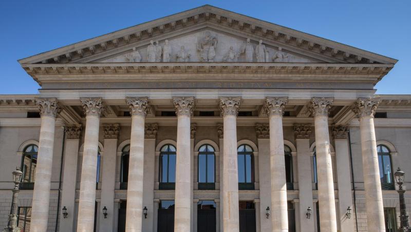 Passanten sitzen auf der Treppe vor der Bayerischen Staatsoper.