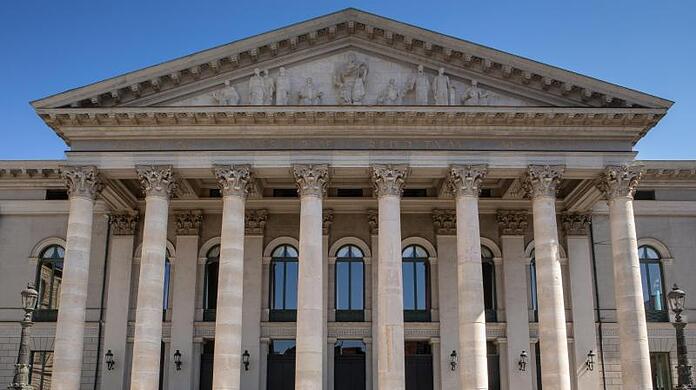 Passanten sitzen auf der Treppe vor der Bayerischen Staatsoper.
