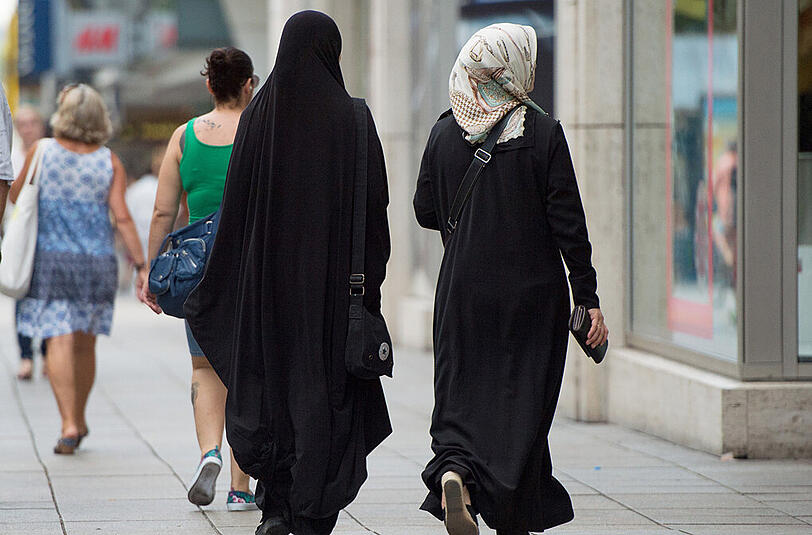 Zwei Frauen mit Kopftuch und langer Oberbekleidung laufen über die Königstraße in Stuttgart.