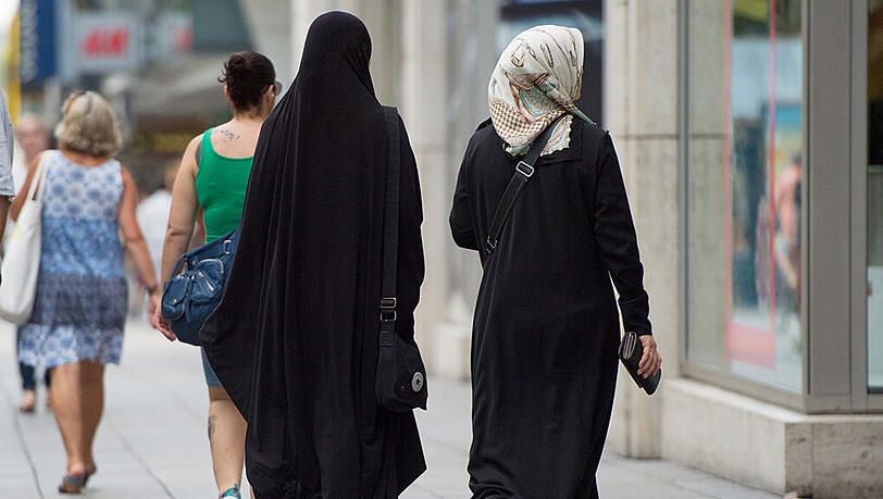 Zwei Frauen mit Kopftuch und langer Oberbekleidung laufen über die Königstraße in Stuttgart. Zwei Frauen mit Kopftuch und langer Oberbekleidung laufen über die Königstraße in Stuttgart.