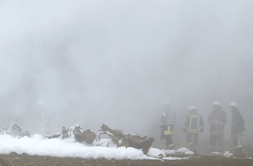 Feuerwehrmänner stehen am ausgebrannten Wrack eines zweistrahligen Geschäftsflugzeugs, das am Sonntag auf dem Gelände einer Mülldeponie bei Rivenich (Rheinland-Pfalz) in Löschschaum liegt.