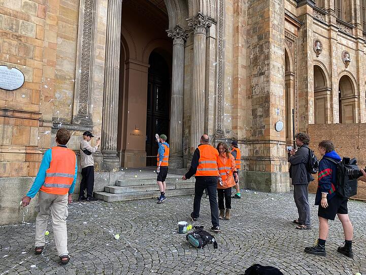 Mit in weiße Farbe getunkten Tennisbällen protestieren Aktivisten der "Letzten Generation" am Mittwoch am Maximilianeum in München.