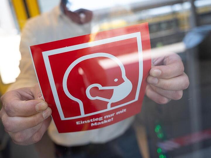 Ein mann befestigt ein Informationsschild zur Maskenpflicht. Foto: Sebastian Gollnow/dpa/Symbolbild