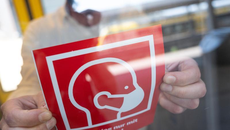 Ein mann befestigt ein Informationsschild zur Maskenpflicht. Foto: Sebastian Gollnow/dpa/Symbolbild
