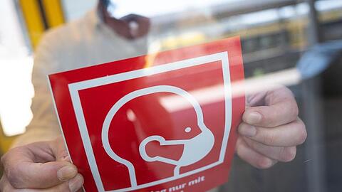 Ein mann befestigt ein Informationsschild zur Maskenpflicht. Foto: Sebastian Gollnow/dpa/Symbolbild