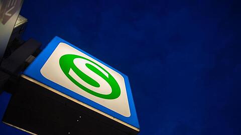 Ein S-Bahn-Schild hängt an einer Station vor dem dunklen Morgenhimmel. Foto: Lino Mirgeler/dpa/Archivbild