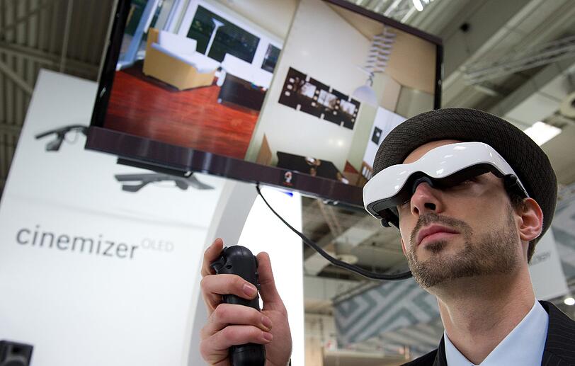 Alle Jahre wieder werden auf der CeBit einige Science-Fiction-Ideen verwirklicht. Diese Brille ermöglicht, durch virtuelle Räume zu gehen. Eine Ahnung davon, was der Träger sieht, vermittelt der Fernseher über ihm.