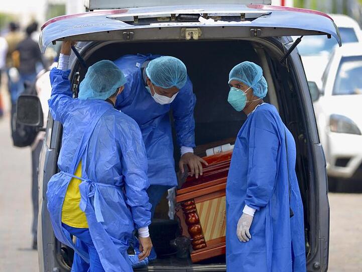 Männer mit Schutzanzügen laden vor einem Krankenhaus in Ecuador einen Sarg in einen Wagen.