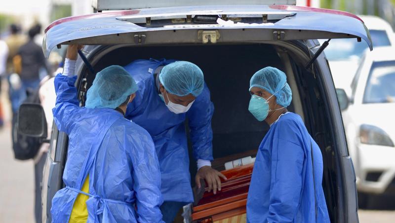 Männer mit Schutzanzügen laden vor einem Krankenhaus in Ecuador einen Sarg in einen Wagen. Männer mit Schutzanzügen laden vor einem Krankenhaus in Ecuador einen Sarg in einen Wagen.