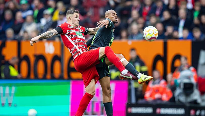 Augsburgs Jeffrey Gouweleeuw (l) in Aktion gegen Wolfsburgs Lukas Nmecha (r).
