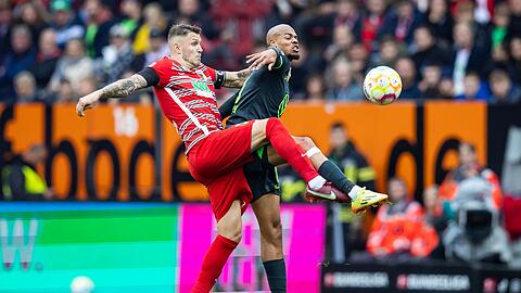 Augsburgs Jeffrey Gouweleeuw (l) in Aktion gegen Wolfsburgs Lukas Nmecha (r).