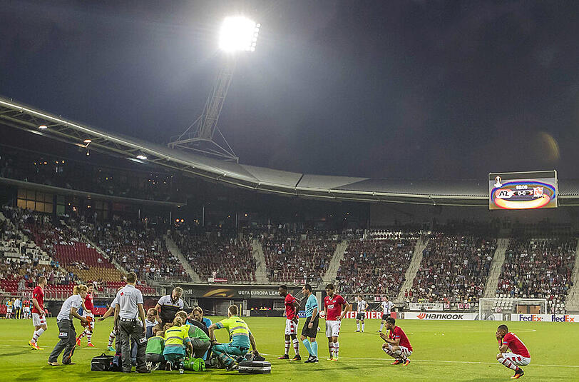 Dramatische Momente in Alkmaar: Sanitäter kümmern sich um den bewusstlos am Boden liegenden Stjin Wuytens, MItspieler hocken entsetzt daneben.