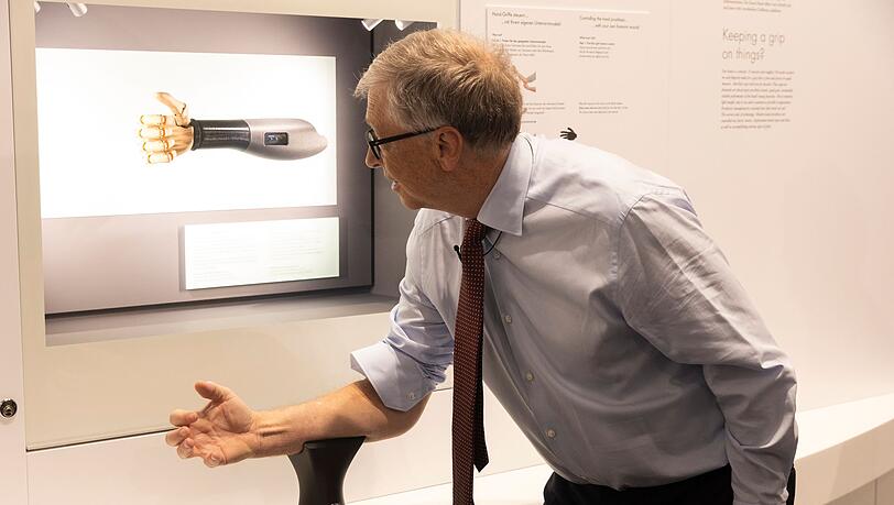 Bill Gates probiert im Deutschen Museum eine Handprothese aus, die sich über die Armmuskeln steuern lässt.